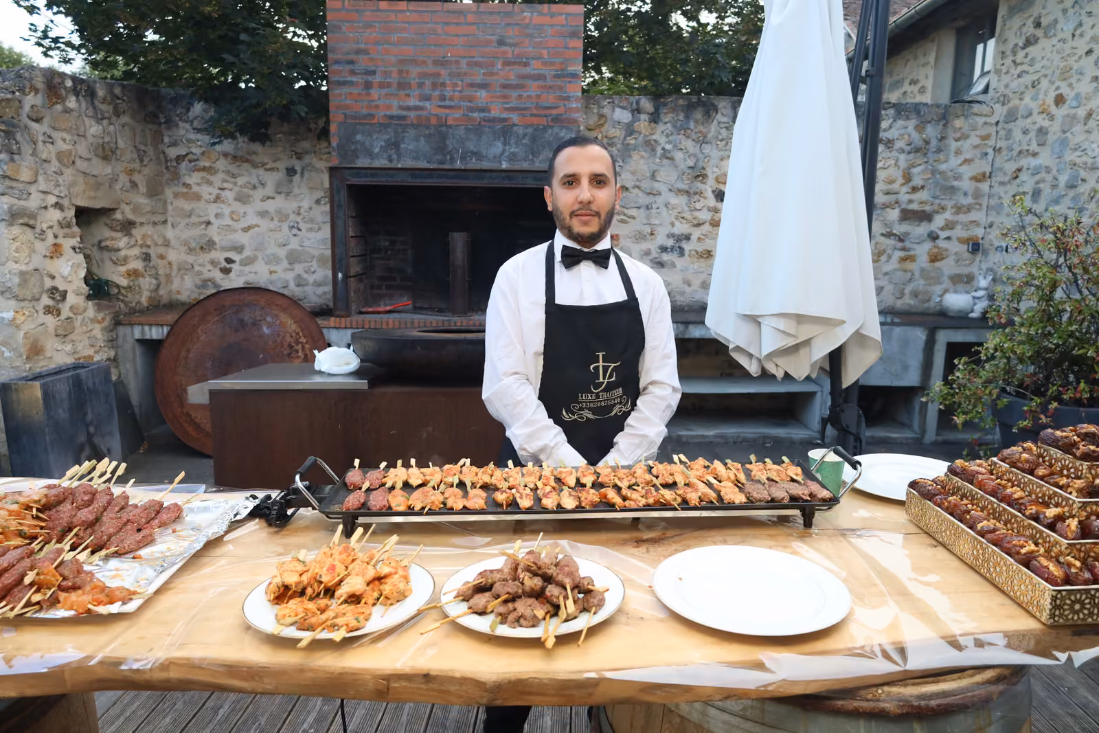 Serveur en tablier derrière un atelier plancha de brochettes de poulet et de kefta en extérieur
