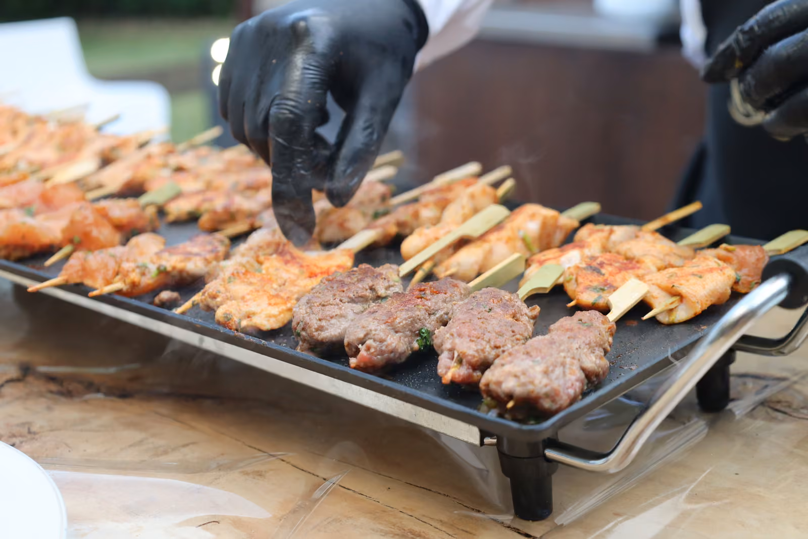 Main gantée retournant des brochettes de poulet et de kefta sur une plancha