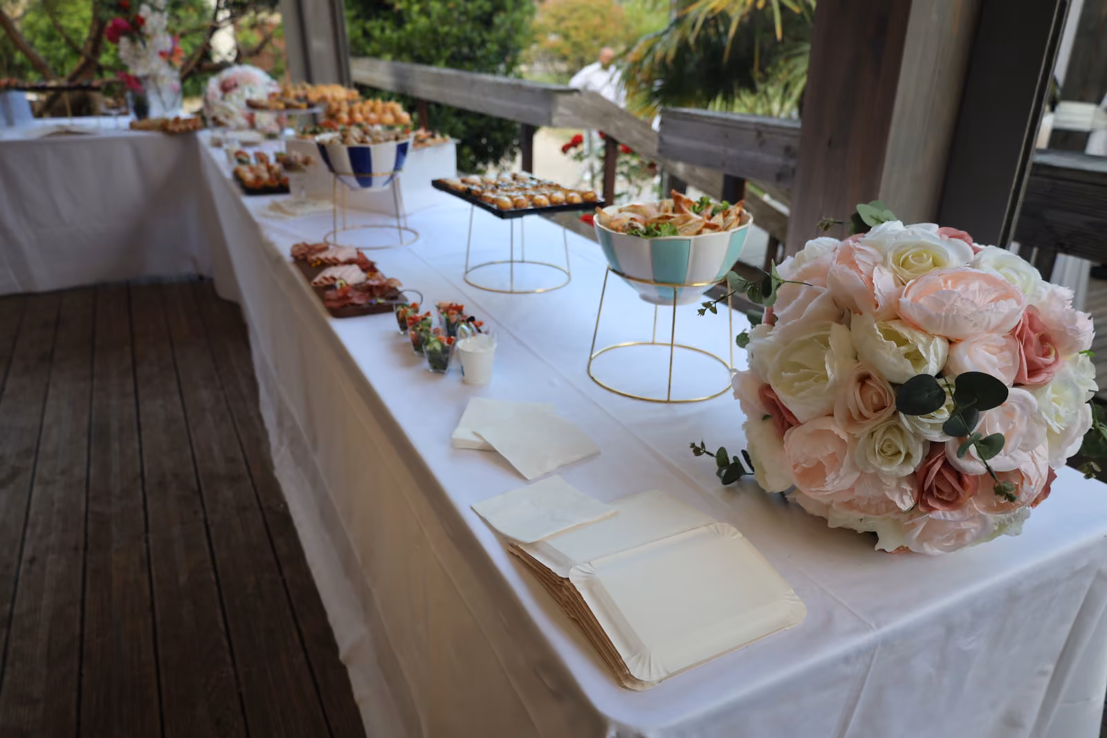 Long buffet nappé de blanc en terrasse, bouquet de roses blanches et roses au premier plan