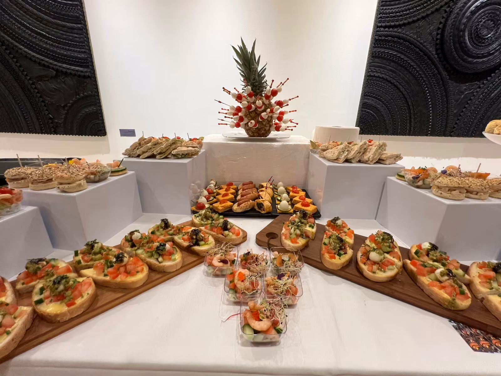 Buffet dînatoire en salle : pyramide d'ananas décorée, canapés sur planches et verrines de crevettes