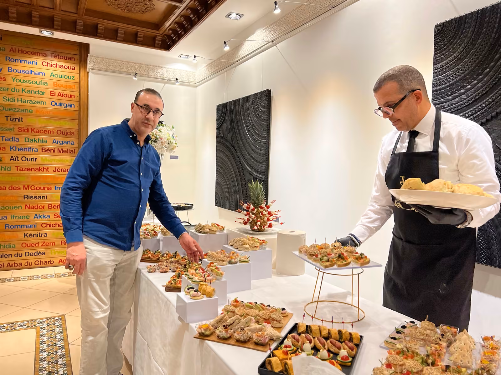 Mise en place du buffet Chef traiteur et serveur en tablier noir et gants dressant ensemble un buffet de réception