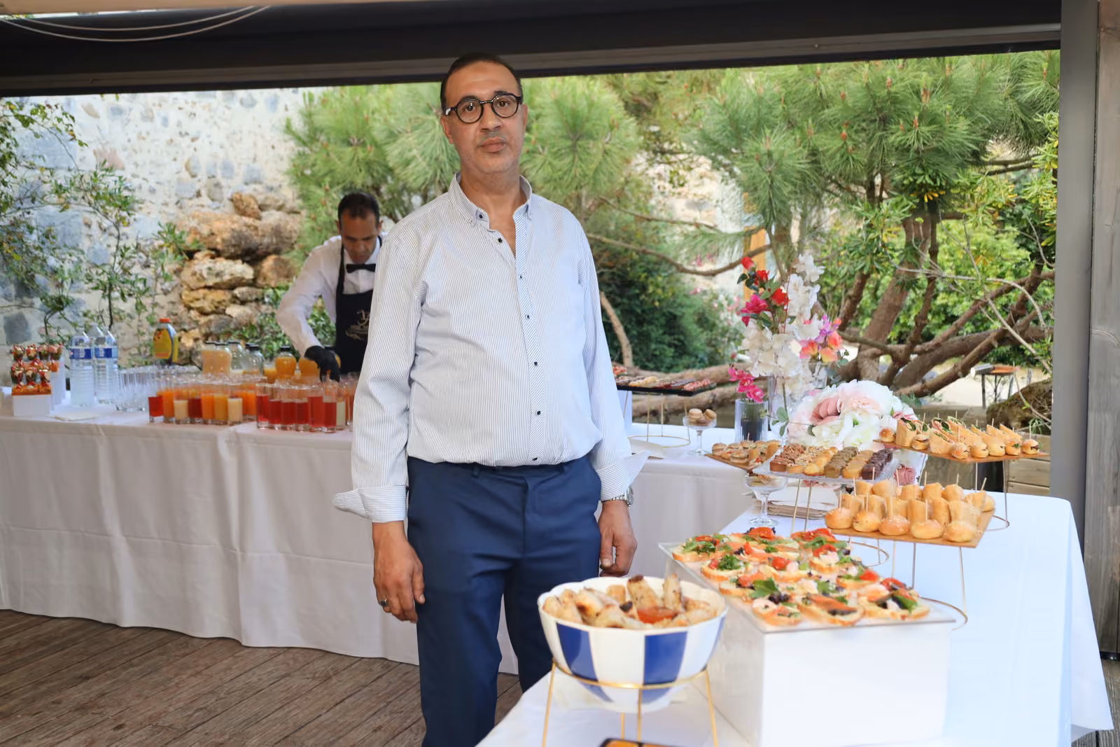 Chef traiteur en chemise blanche debout devant le buffet du cocktail en terrasse