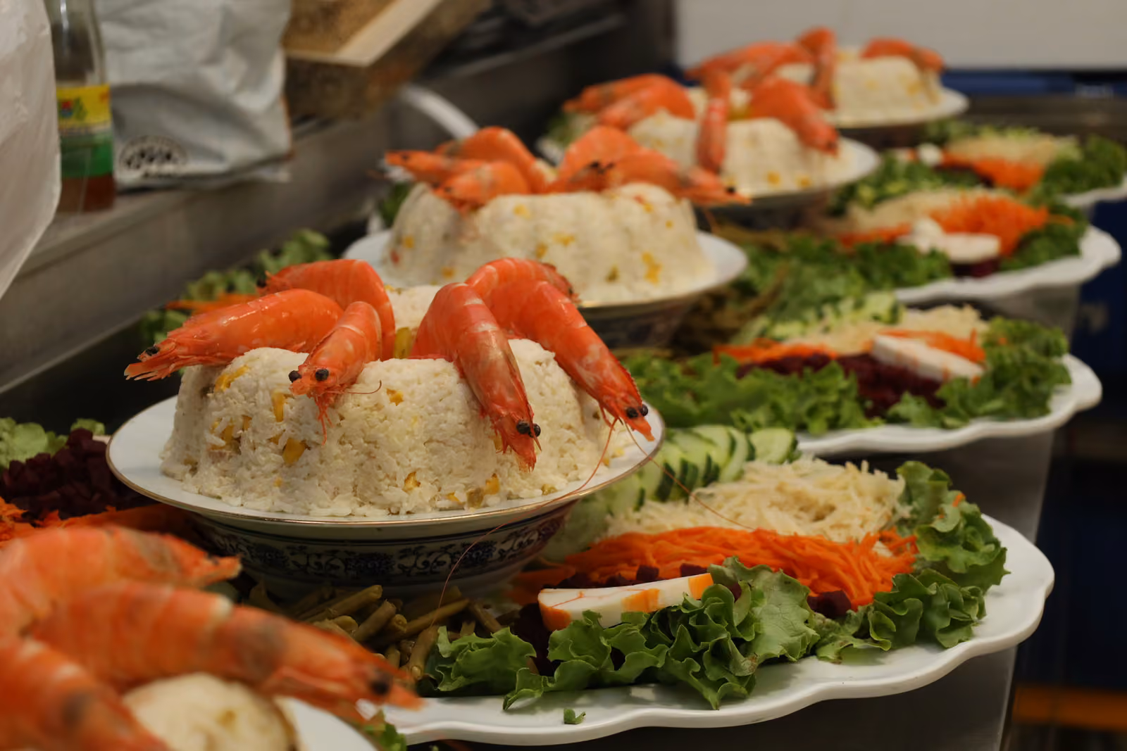 Couronnes de riz garnies de crevettes entières sur lit de salade et crudités, alignées en cuisine
