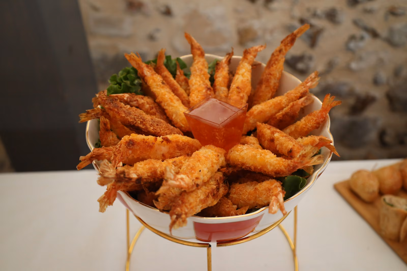 Coupe de crevettes panées en couronne autour d'une sauce, sur un présentoir doré