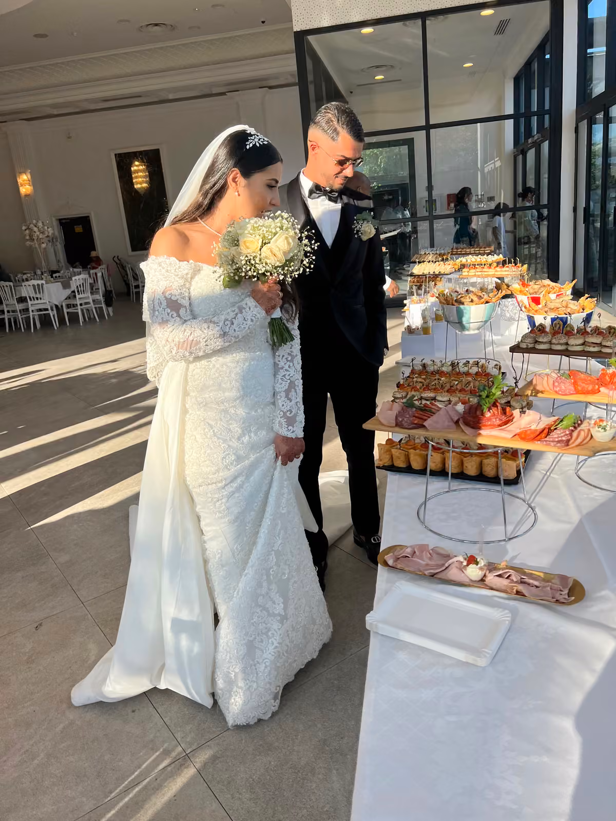 Mariés en robe blanche et costume noir découvrant le buffet du traiteur