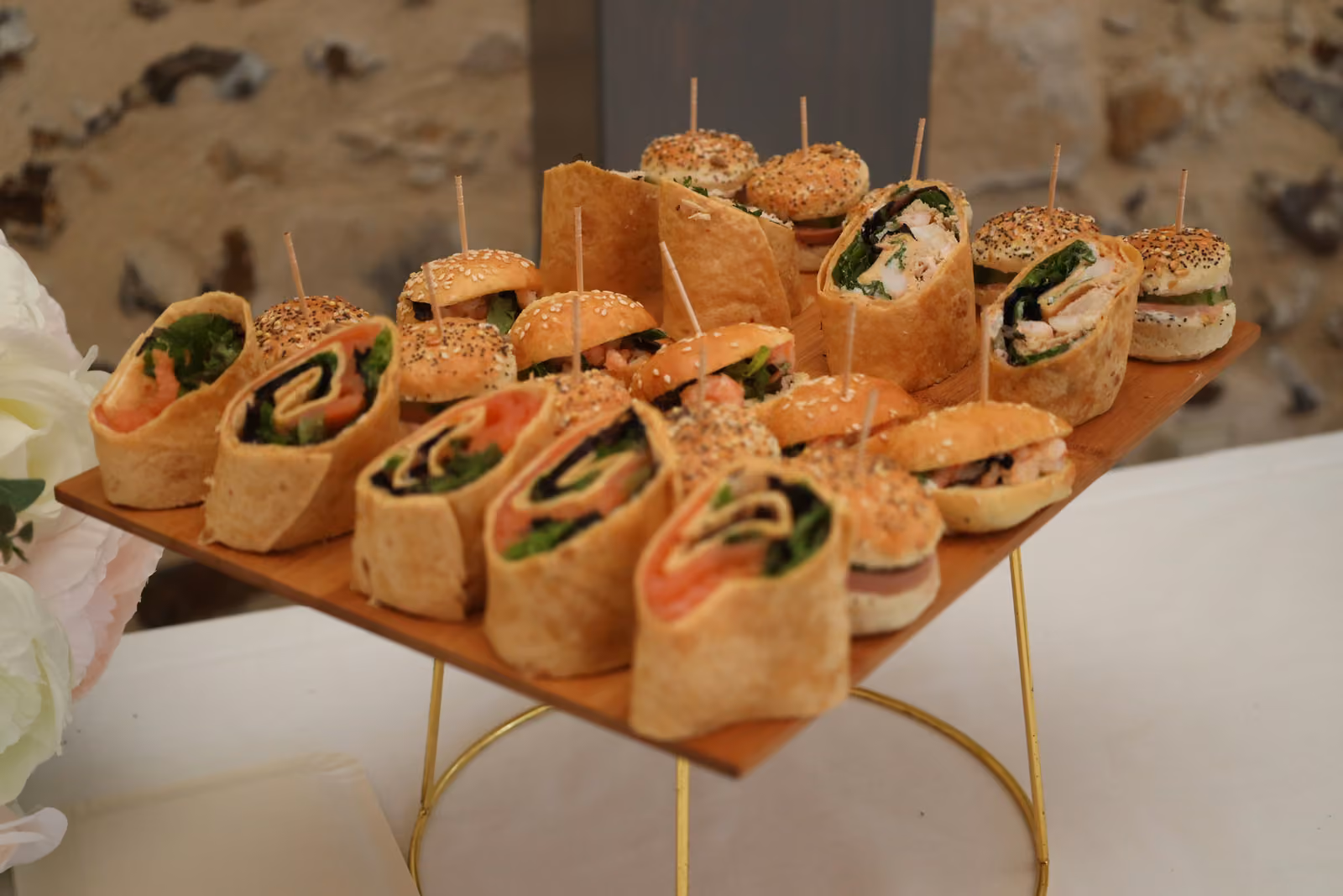 Plateau en bois de mini-burgers au sésame et wraps au saumon sur un présentoir doré