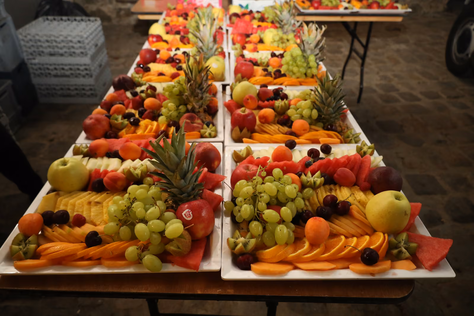 Rangées de plateaux de fruits frais découpés : raisin, ananas, orange, pomme et pastèque