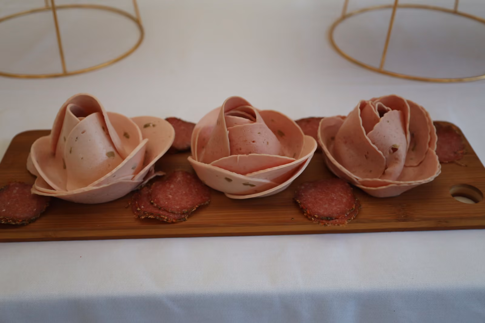Roses de jambon et rondelles de saucisson disposées sur une planche en bois