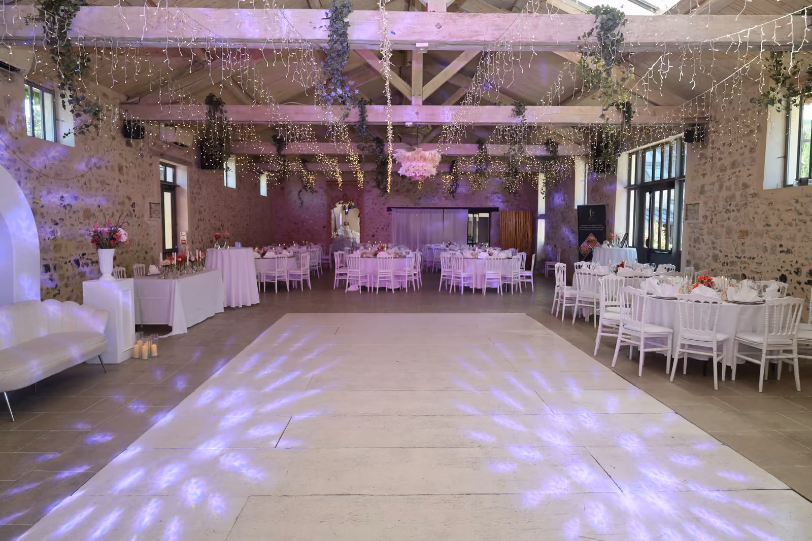 Salle de réception de mariage en pierre et poutres apparentes, piste de danse blanche et tables dressées
