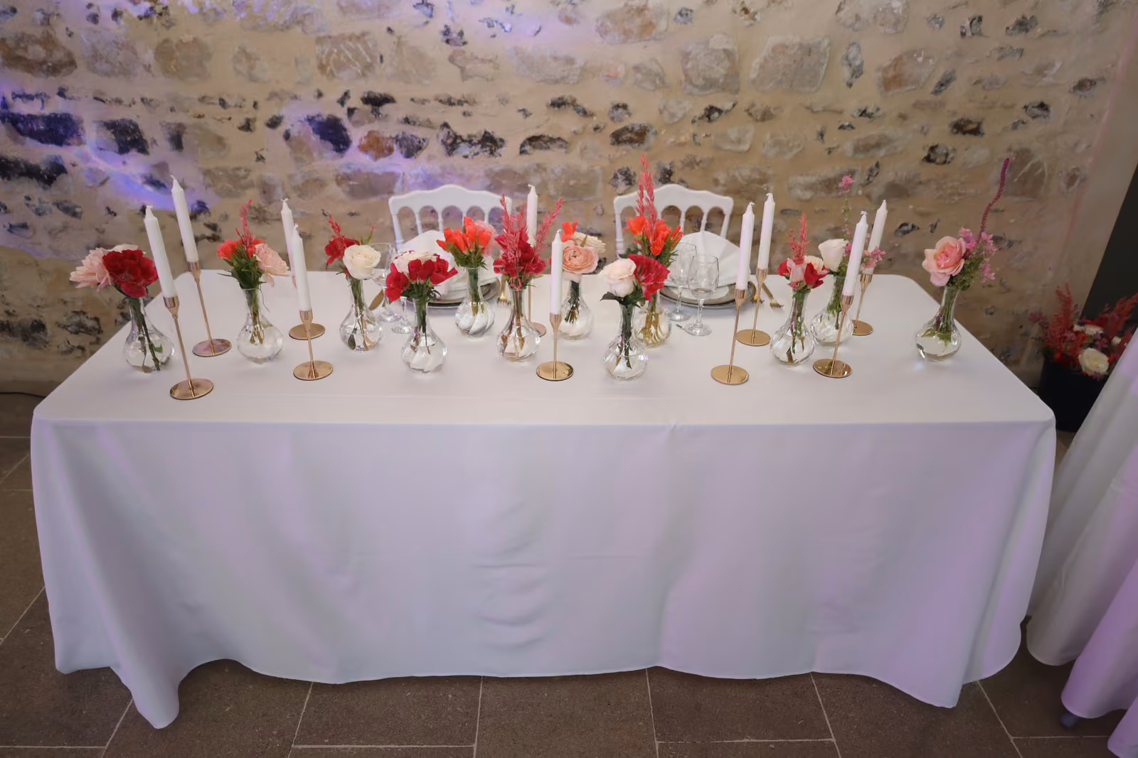 Table d'honneur de mariage fleurie Table d'honneur de mariage nappée de blanc, soliflores rouges et roses, chandeliers dorés et bougies