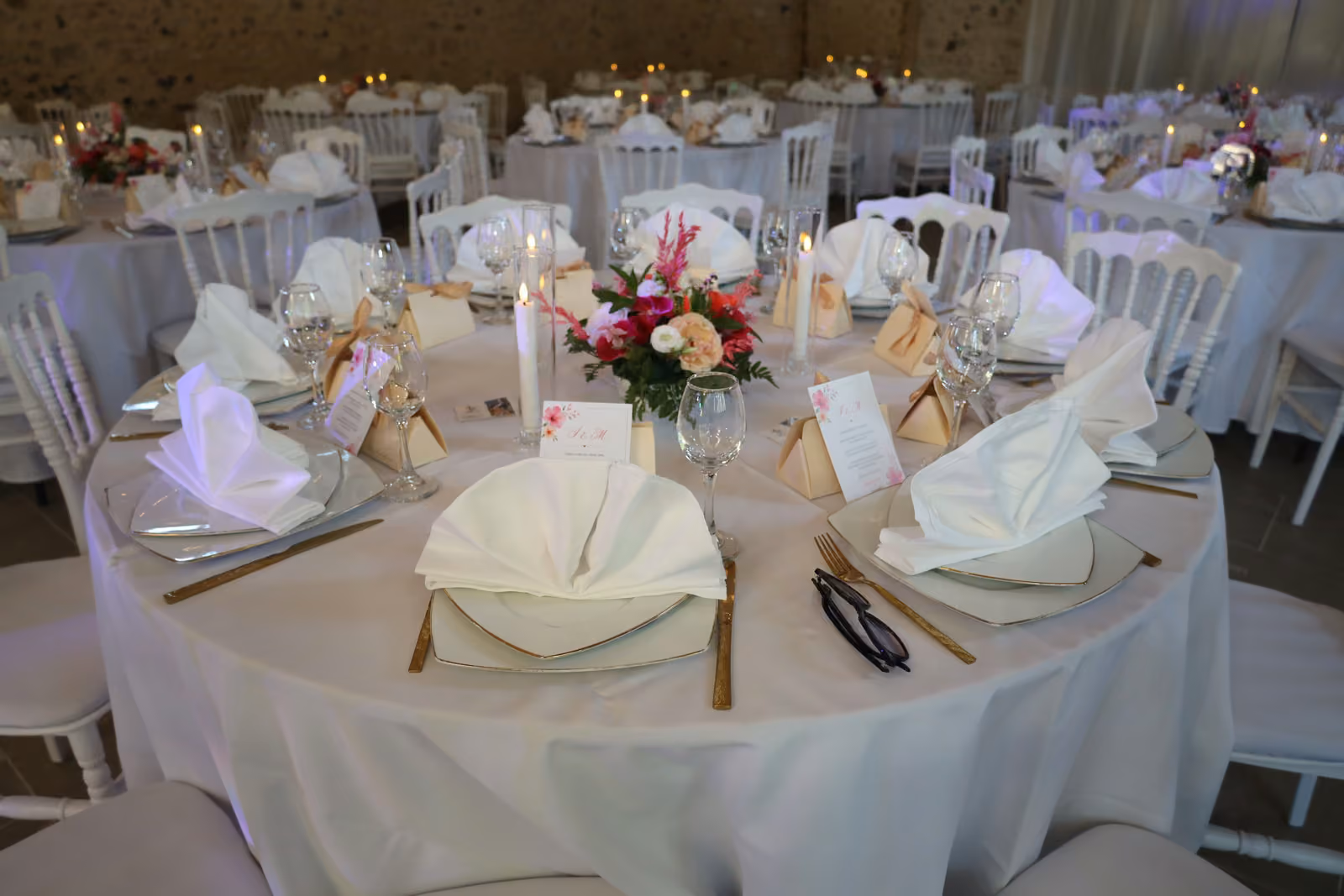 Table d'invités de mariage avec bouquet rose, bougies, verres à pied et petites boîtes cadeaux