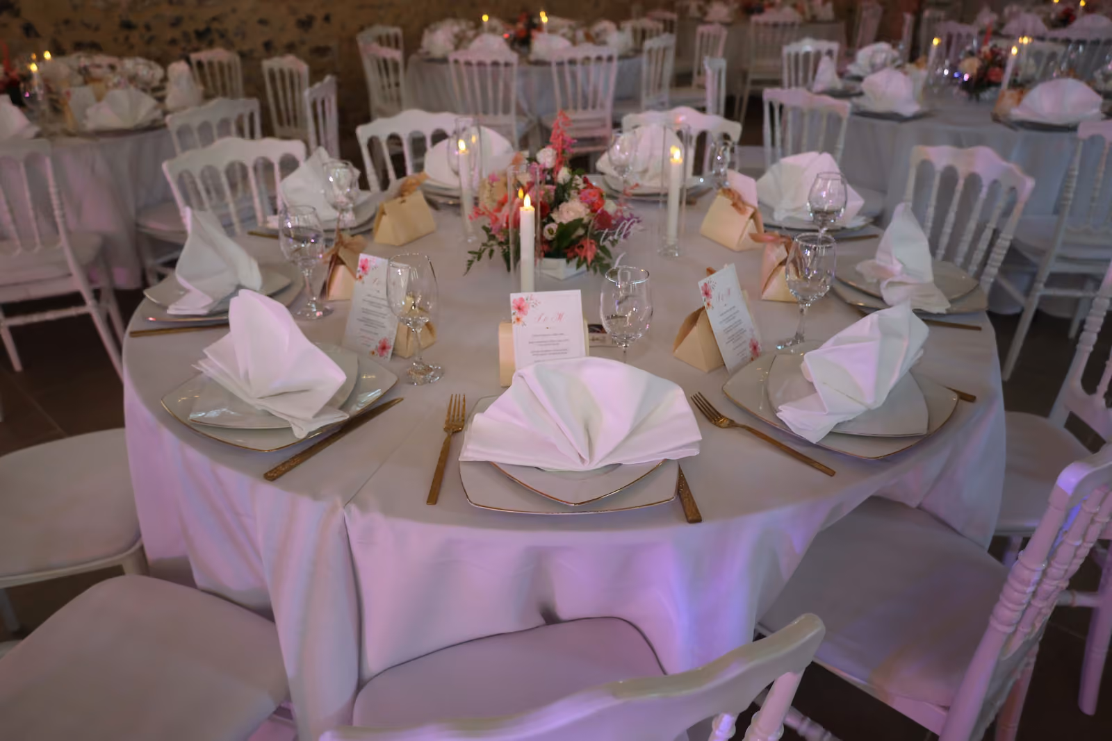 Table d'invités dressée pour un mariage Table ronde de mariage dressée : serviettes pliées en éventail, assiettes, couverts dorés et bouquet central