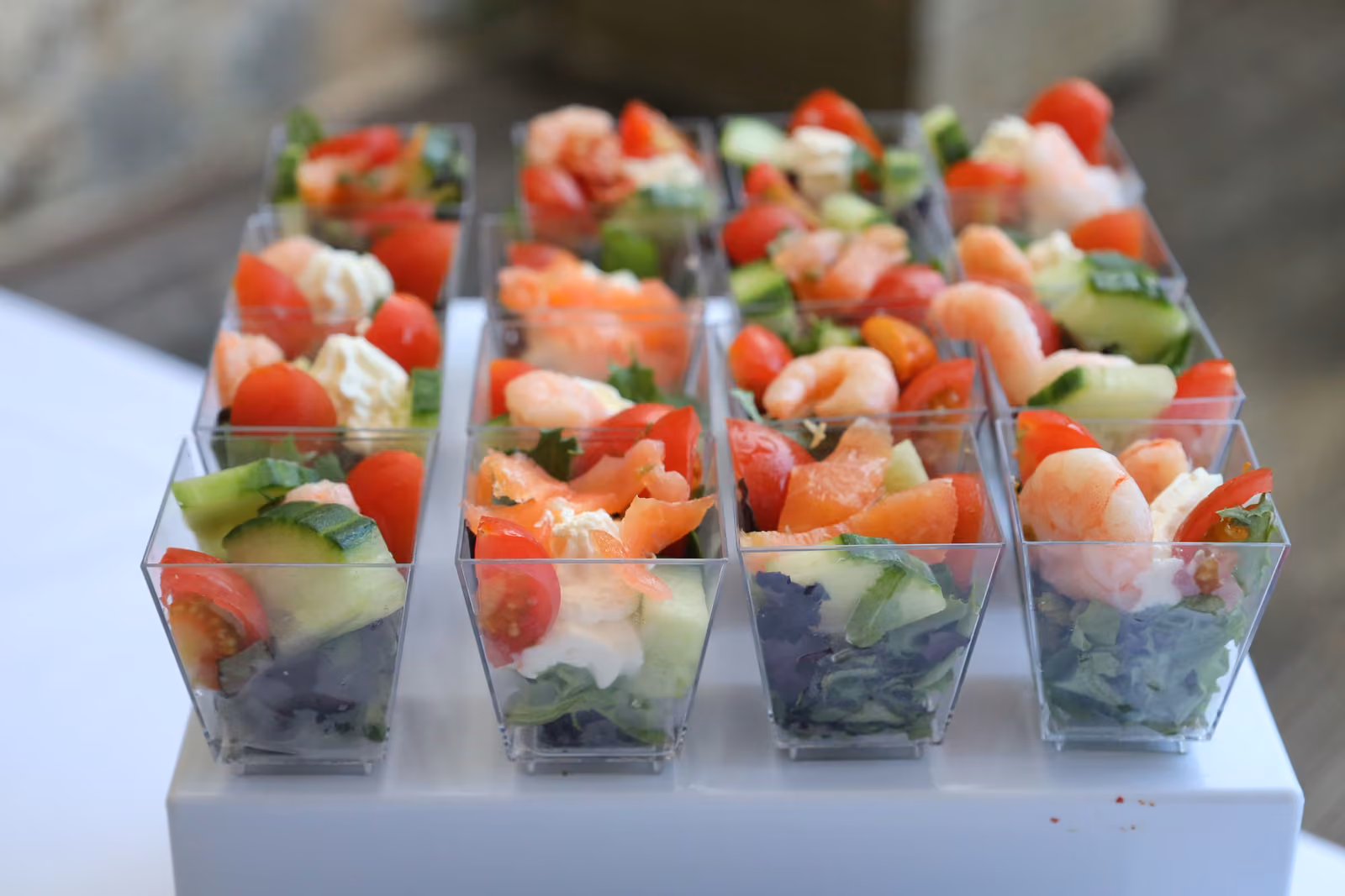 Verrines apéritives aux crevettes, saumon, tomates cerises et concombre sur un présentoir blanc