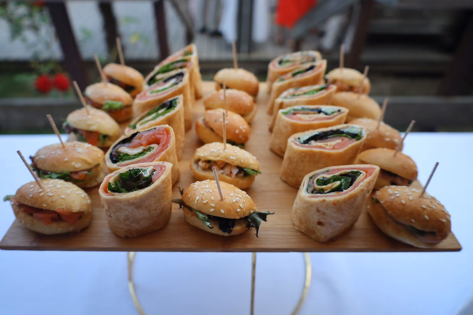 Plateau en bois de wraps roulés et de mini-burgers sur pics, sur un présentoir doré